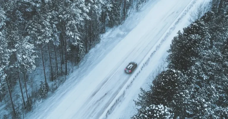 Car driving down a foreststreet in the winter between trees photographed from above