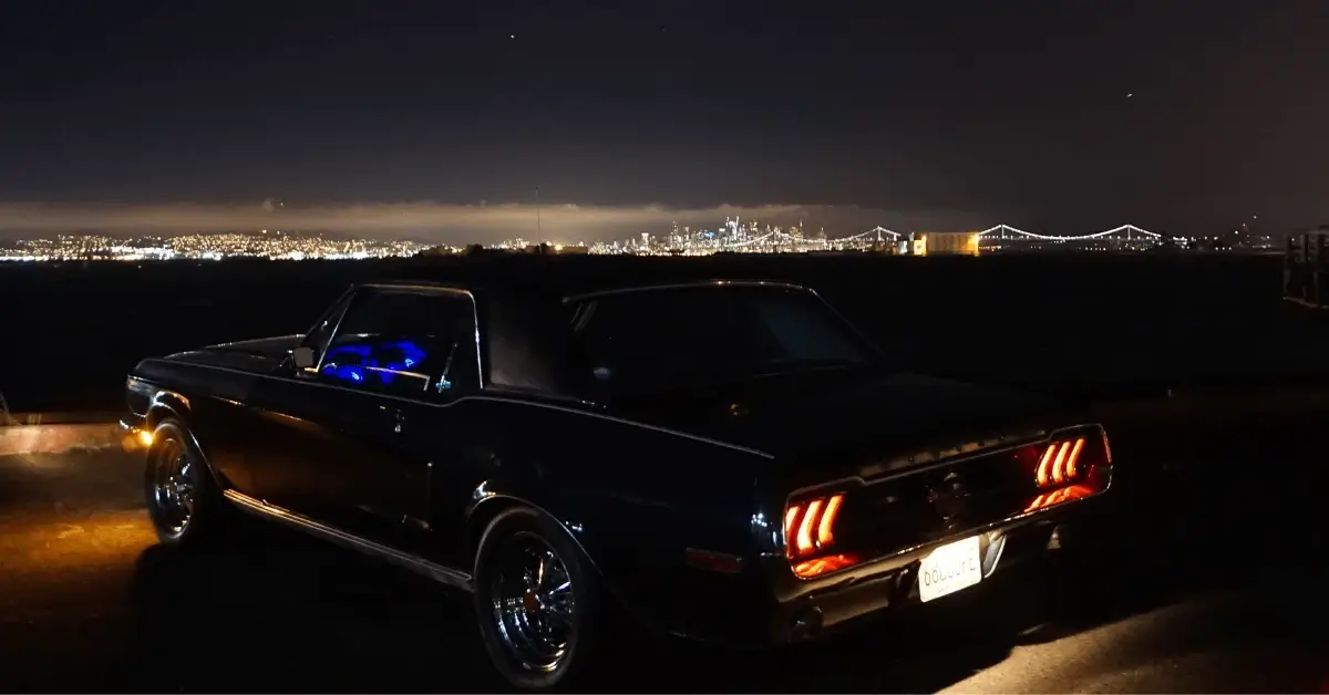 69 Mustang standing on a mountain in front of a city at night