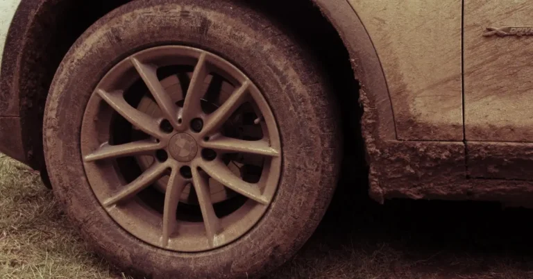 The front left wheel on a car which is full of mud and dirt