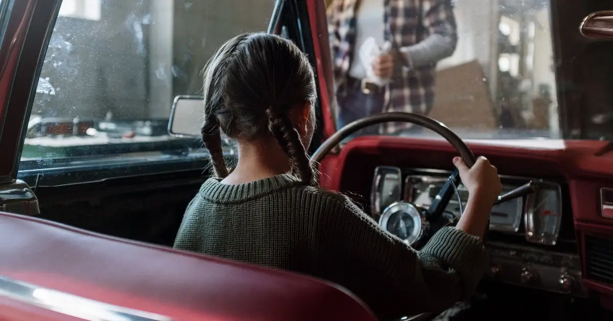 Little Girl sitting on the drivers seat of an old car
