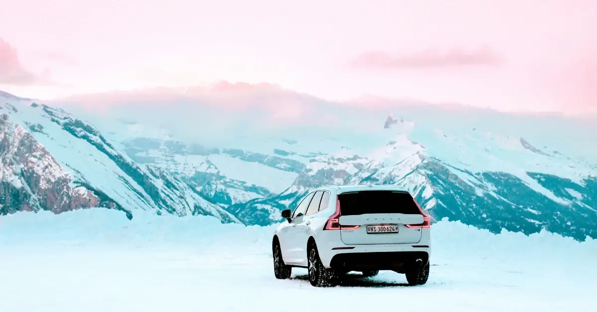 A white Volvo XC 60 standing towards snowy mountains and an rose sky