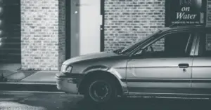 An old damaged car standing in front of a wall photographed in Black and White