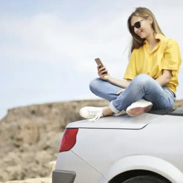 A girl sitting on her trunk checking her phone with the Ocean in the background