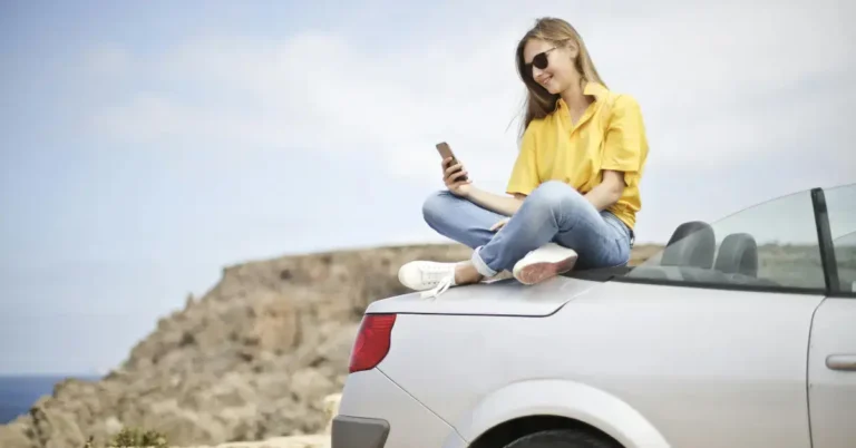 A girl sitting on her trunk checking her phone with the Ocean in the background
