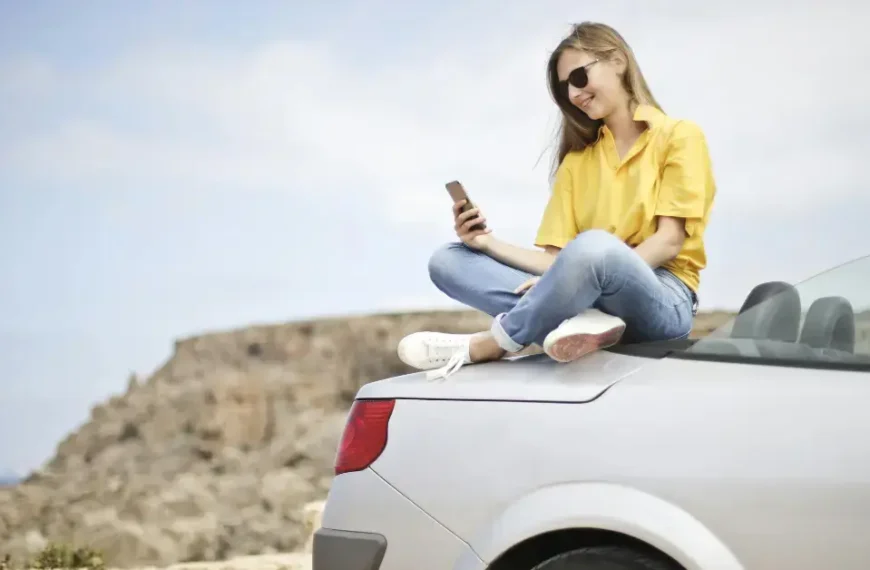 A girl sitting on her trunk checking her phone with the Ocean in the background