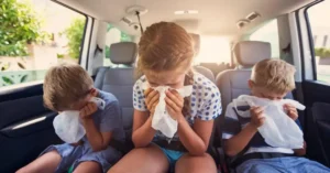 Three children on abackseat of a car, vomiting in a paperbag