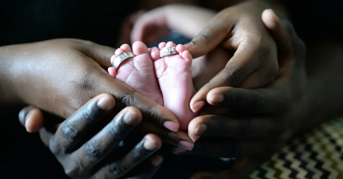 THe hands from Father and Mother holding the feet of their newborn