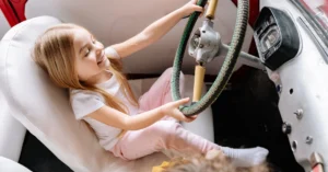 A young Girl is holding the steering wheel of a car