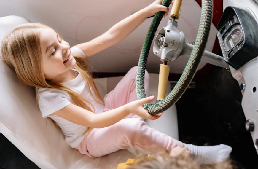 A young Girl is holding the steering wheel of a car