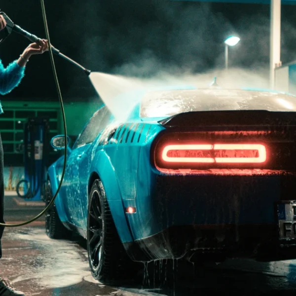 A woman is pressure washing her car at night