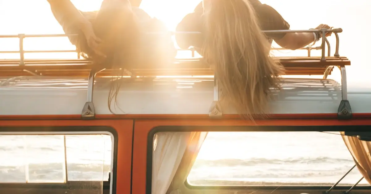 Two Students lying on the top of a Camping Bus with the sun shining in the background