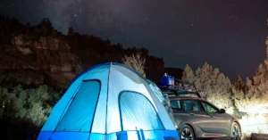 A enlighted Tent behind a Car under the Starsky