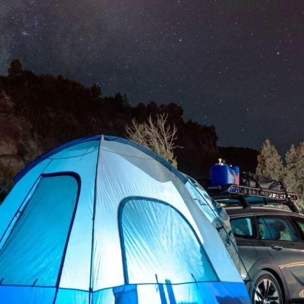 A enlighted Tent behind a Car under the Starsky