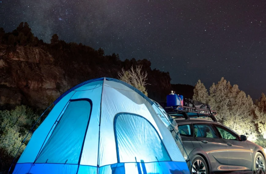 A enlighted Tent behind a Car under the Starsky