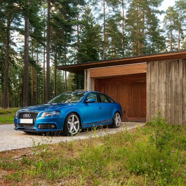 A turkis Audi A4 on a Driveway in front of a Forest House