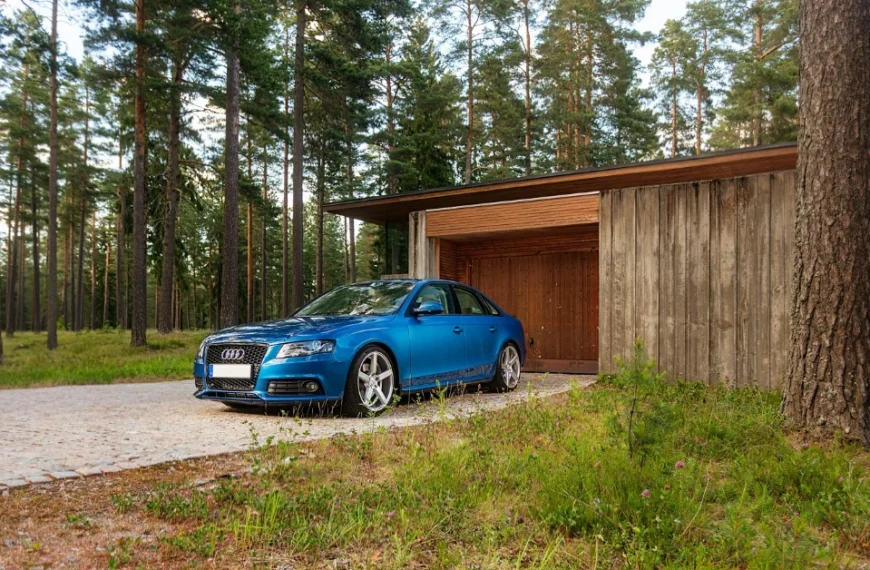 A turkis Audi A4 on a Driveway in front of a Forest House