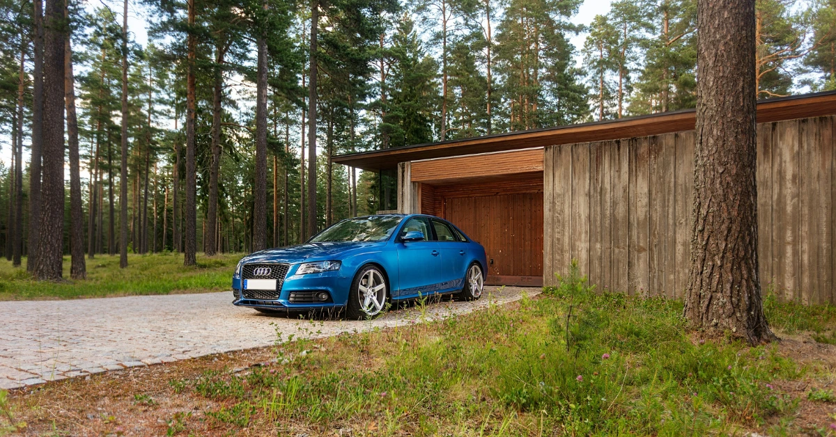 A turkis Audi A4 on a Driveway in front of a Forest House